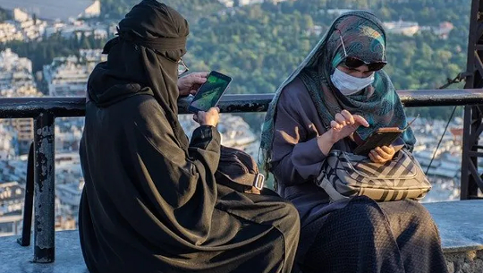 two Muslim women wearing the niqab and using their cell phones