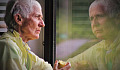 older person eating an apple and looking at her reflection in a window